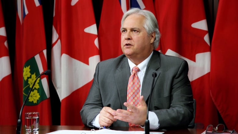 A provincial official speaks at a news conference with a row of flags behind him.