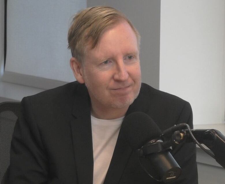 A smiling man sits behind a microphone.