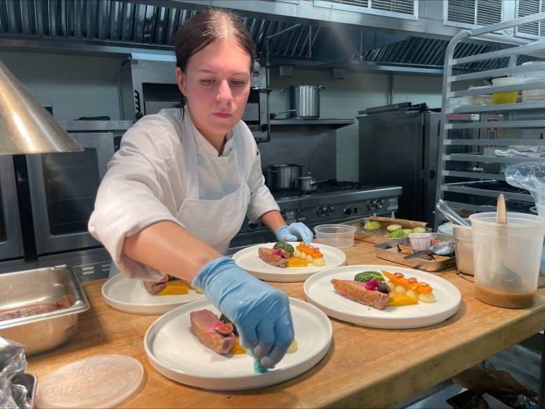 A chef prepares several plates of food in an industrial kitchen.