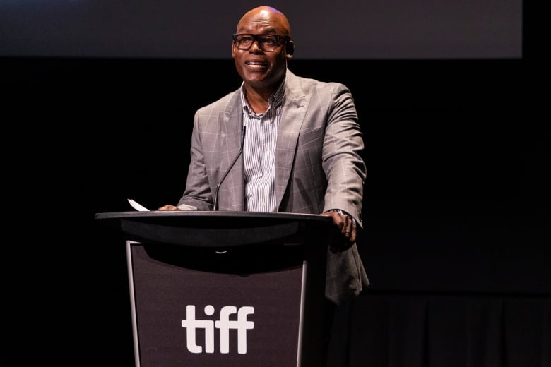 A man in a sport coat speaks at a podium with the TIFF logo. 