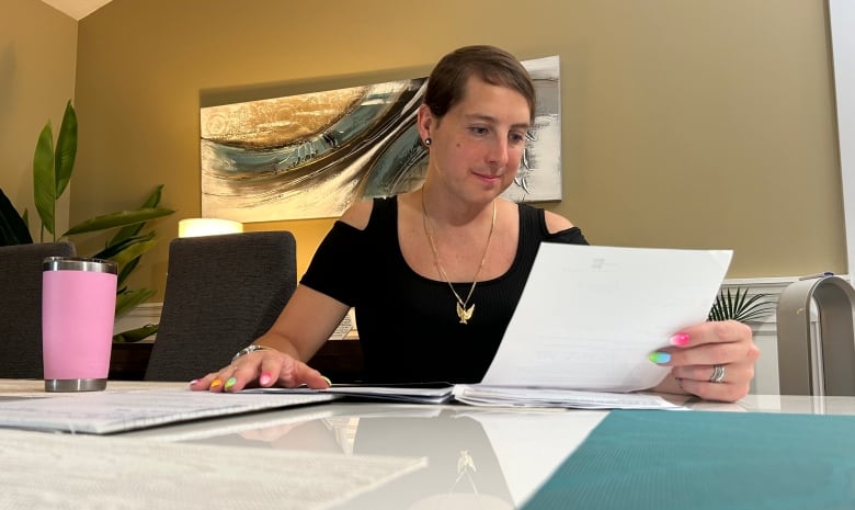 A woman with colourful nails looks at a piece of paper.