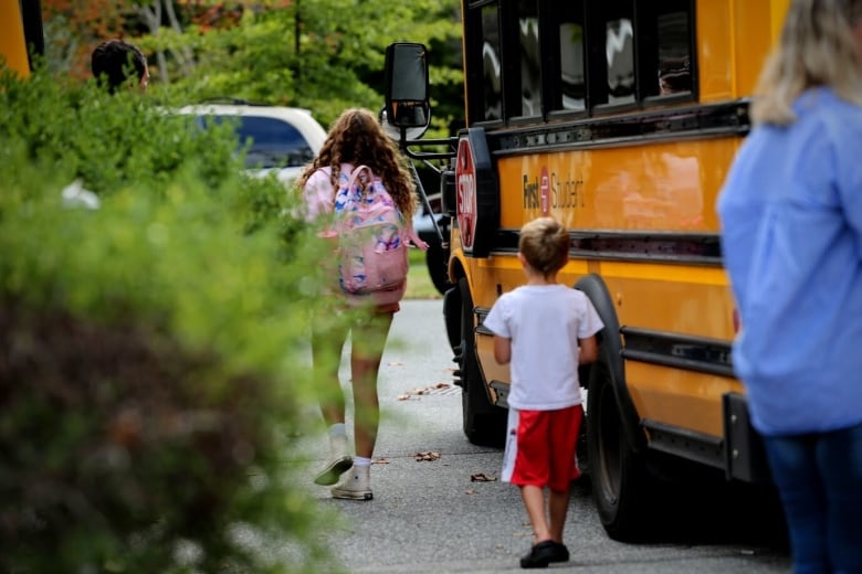 Two children walk by  a  school bus