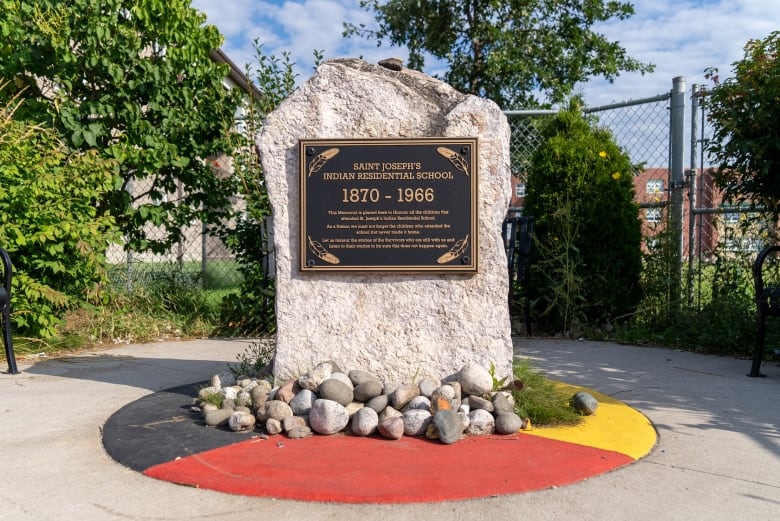 A plaque is seen on a large slab of stone, situated on top of a medicine wheel surrounded by small rocks.