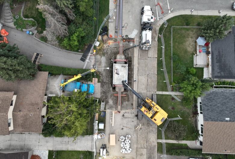 Large construction machines are parked near an excavated section of road, exposing a large pipe.