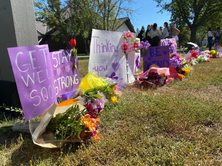 Signs and dozens of bouquets of flowers outside a school yard.