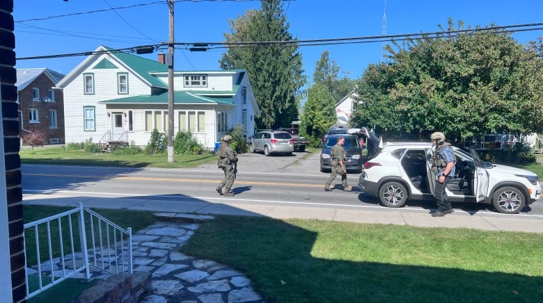 Three police officers stand next to a vehicle with its doors open on a residential street.