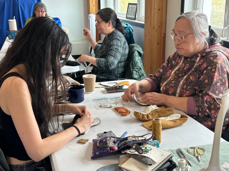 Two women sit at a table sewing together