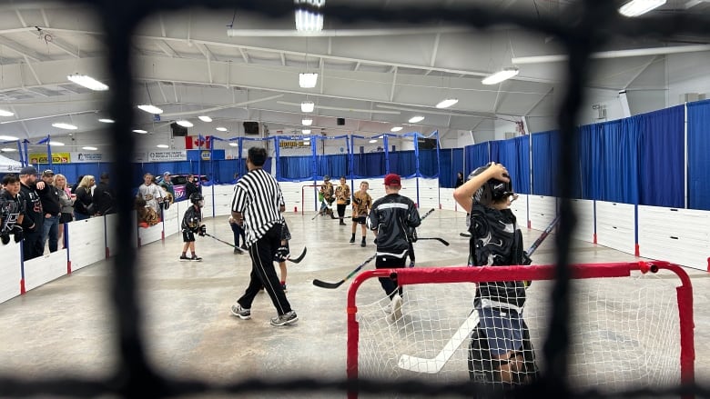 A group of young people play street hockey inside a sporting complex.