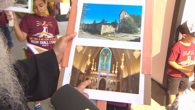 A man's finger points to an image of a church interior with a photo of a burned remains of the same church. 