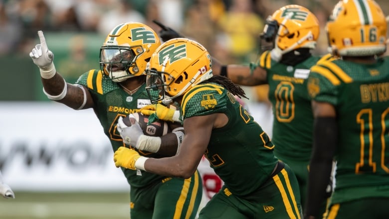 A group of football players in green-and-yellow uniforms celebrate on the field.