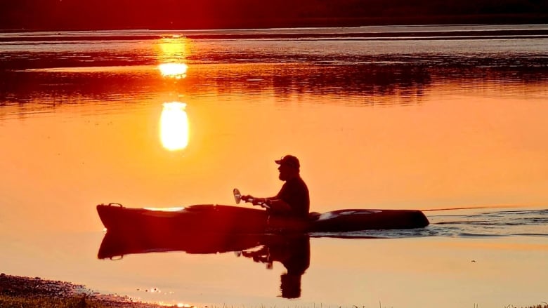 A person canoes through a river glowing in the sunset.