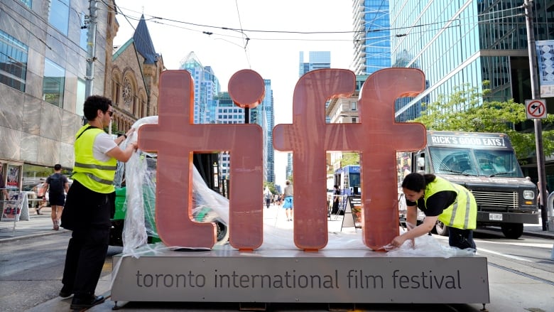 Two people unwrapping plastic from a sign that reads: TIFF.