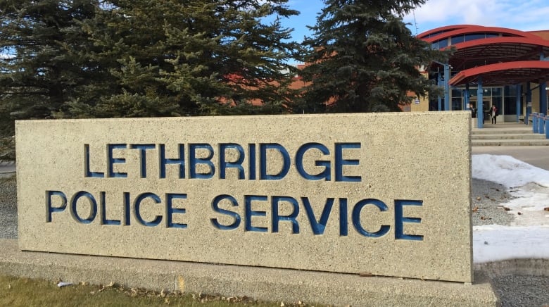 A rectangular slab of rock with Lethbridge Police service carved in blue into it. A building with red roof in the background