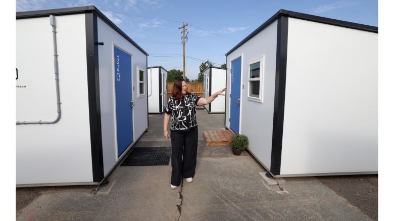 A woamn stands between two small shelters.