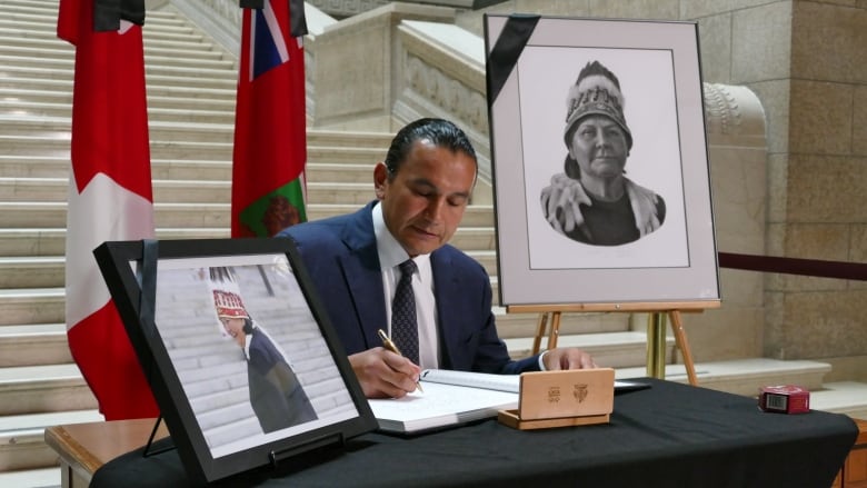 A man sits at a table and signs a page of a book