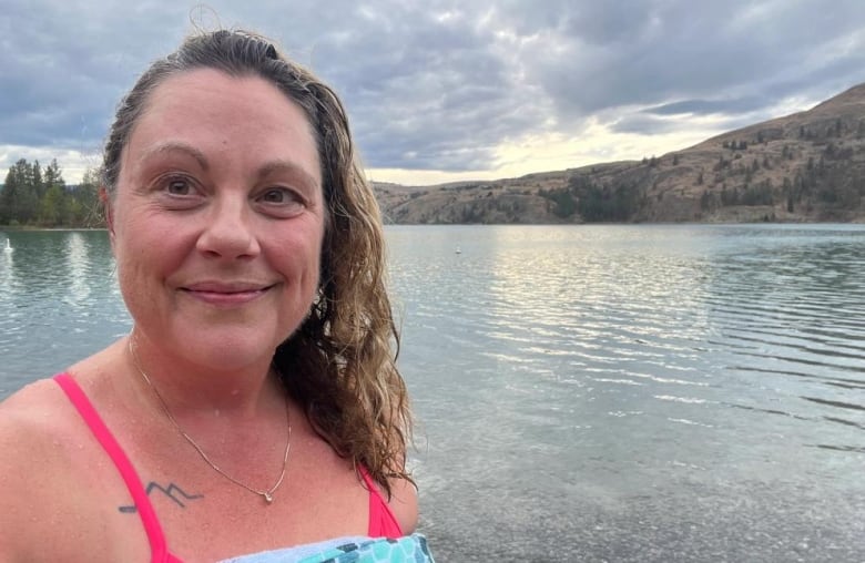 A woman takes a selfie in a swimsuit next to a lake.