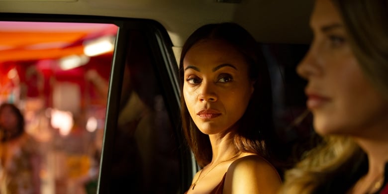 Two women in a car. One looks forward while the other is turned toward her. 