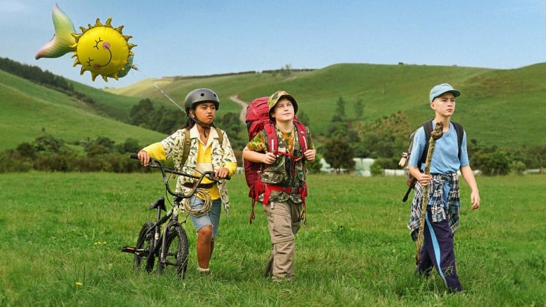 3 kids hiking with a smiley face balloon.