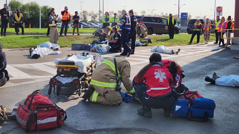 A crowd gathers outside. Paramedics and people in high visibility jackets are among the crowd. Some lay in stretchers on the ground. 