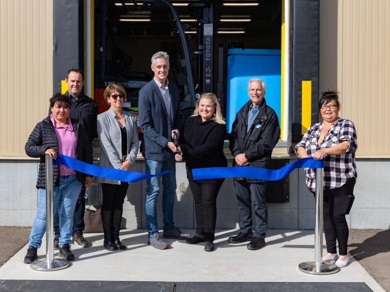 A group of people stand in front of a building, cutting a ribbon.