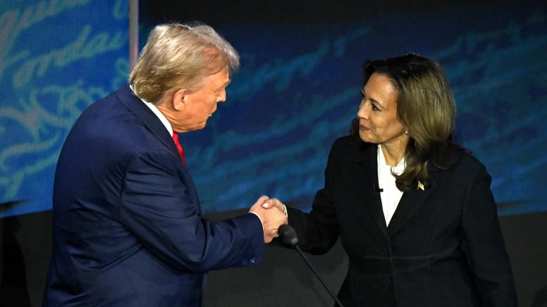 A man and a woman in suits shake hands behind a podium.