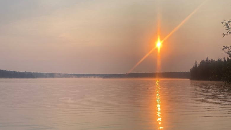 An orange sunrise is seen over a lake