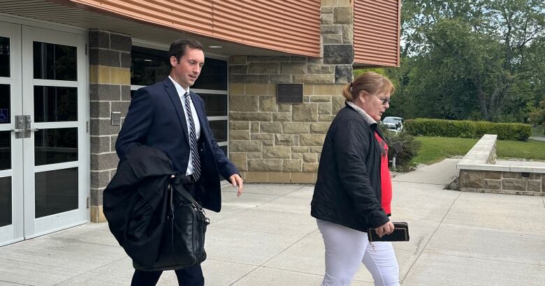 A man in a black suit holding robes walking outside a building with a woman in a jacket walking in front of him.