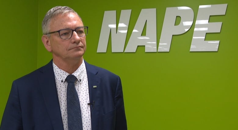 Man in suit stands in front of green wall that says NAPE.