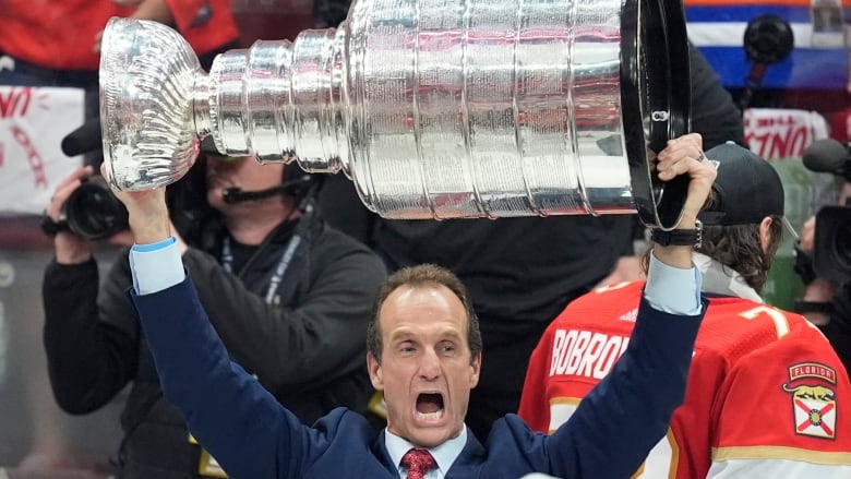 A man in a suit holds the Stanley Cup over his head.