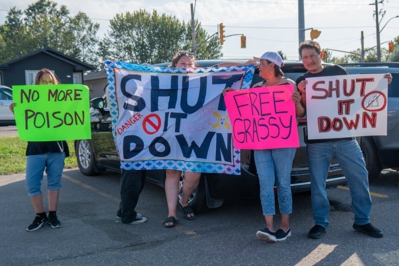 Five people are seen standing in a parking lot, holding signs.