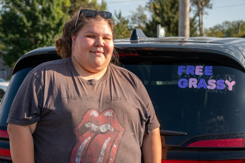 A person wearing a Rolling Stones t-shirt is seen standing beside a vehicle, which has a sign taped to it that says 