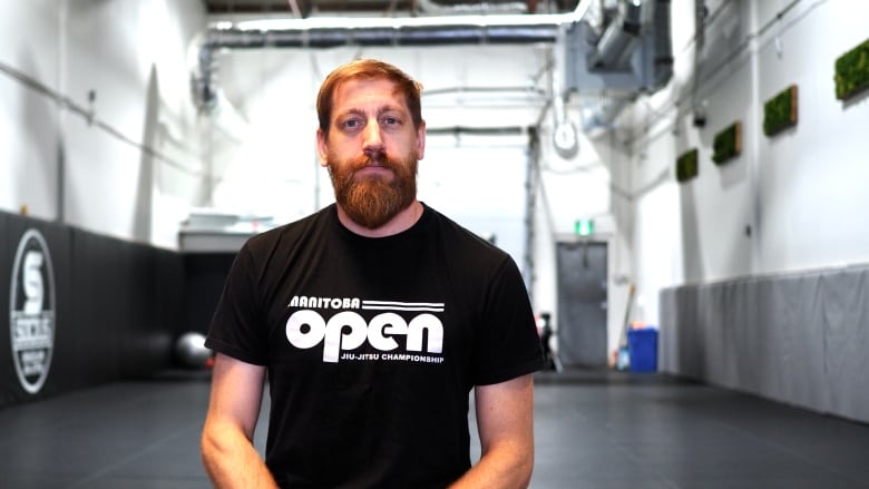 A man in a black T-shirt stands in a gym space.