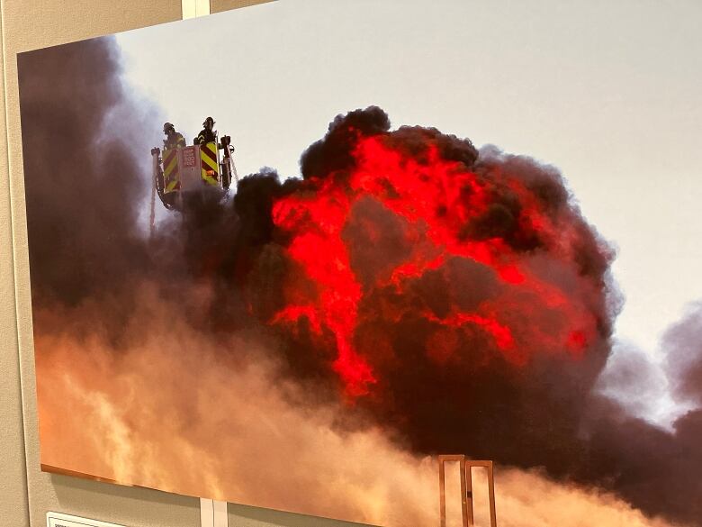 A photo of firefighters on a truck tower overlooking a ball of flames.