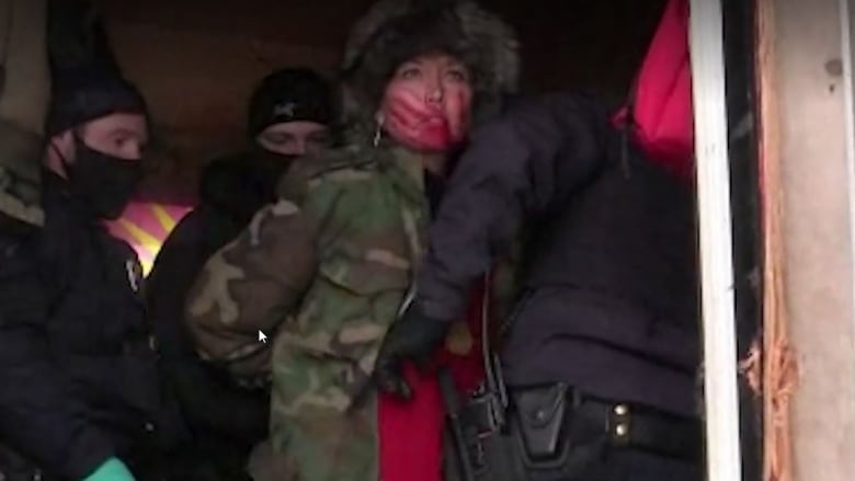 a woman with a red handprint on her face surrounded by police.