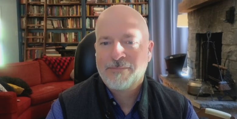 Man with white beard sits in desk chair in living room. 