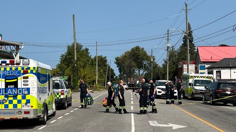 Paramedics stand on a closed-off city street in summer.