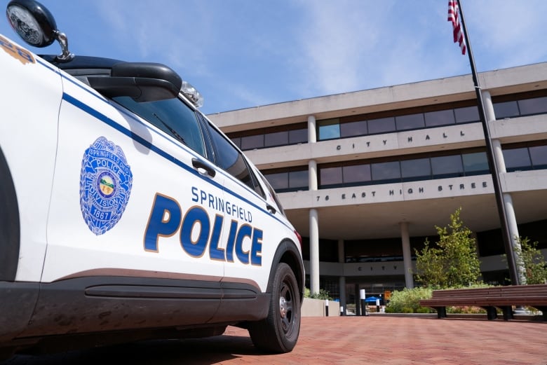 A white police SUV is parked outside a stone city hall building.