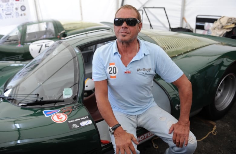 A cleanshaven man wearing sunglasses in a Polo shirt sits in the front seat of a racing car.