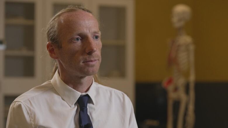 A man in a dress shirt and black tie sits in a laboratory