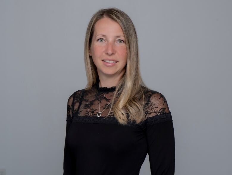 A woman in a black top with blonde hair on a grey background