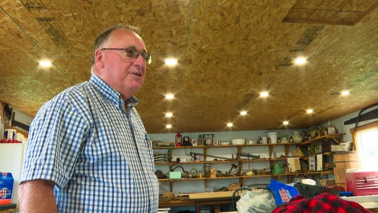 A man with glasses wearing a blue and white plaid shirt looks to the right of the camera.