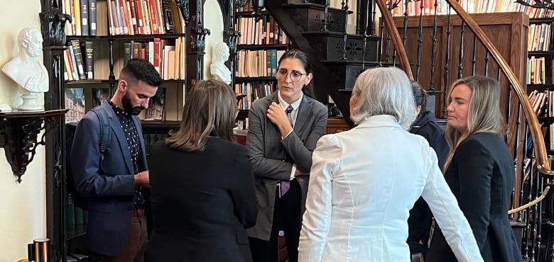 people in blazers stand near a bookcase