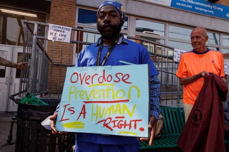 Photo of a man holding a sign reading, 'overdose prevention is a human right.' 