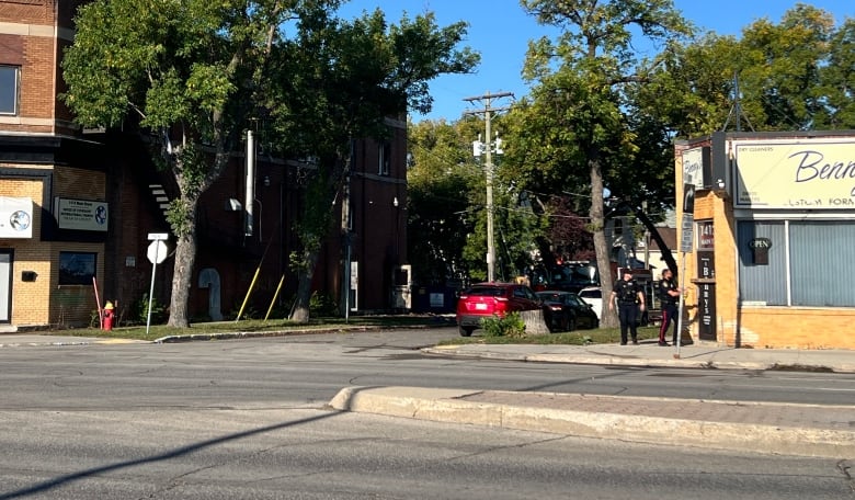 Two police officers walk into a building across the street from a second building that appears charred from a fire. 