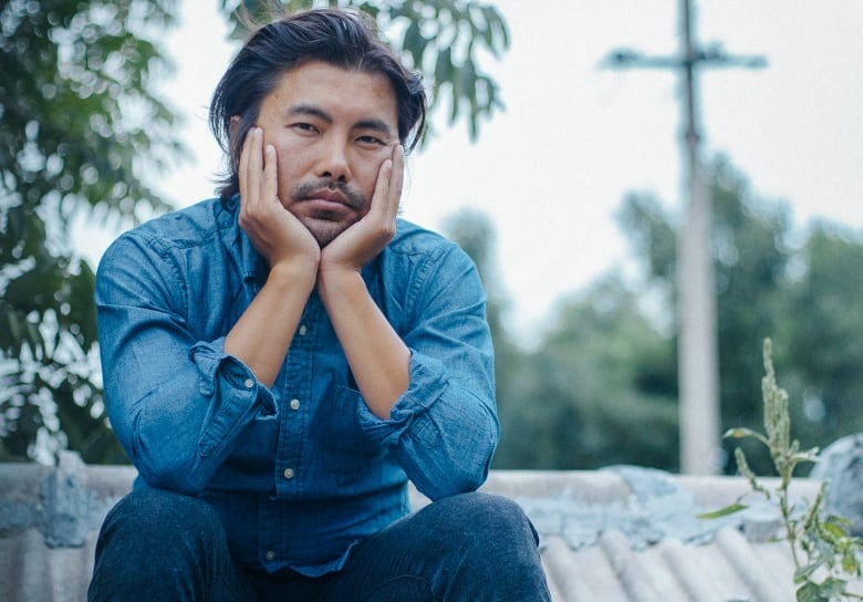 A barefoot man in jeans sits on a terracotta roof.