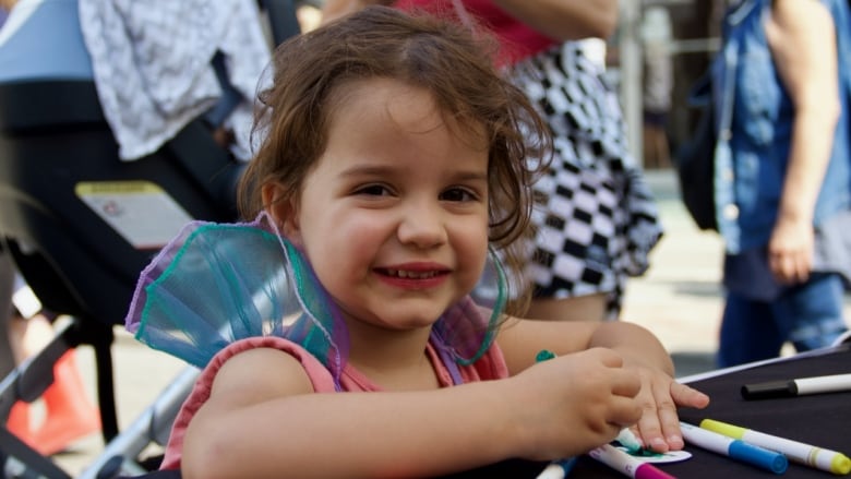 A smiling child colours a piece of paper at a booth outside. 