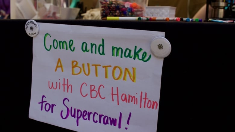 A sign reading 'Come make a button with CBC Hamilton for Supercrawl.'