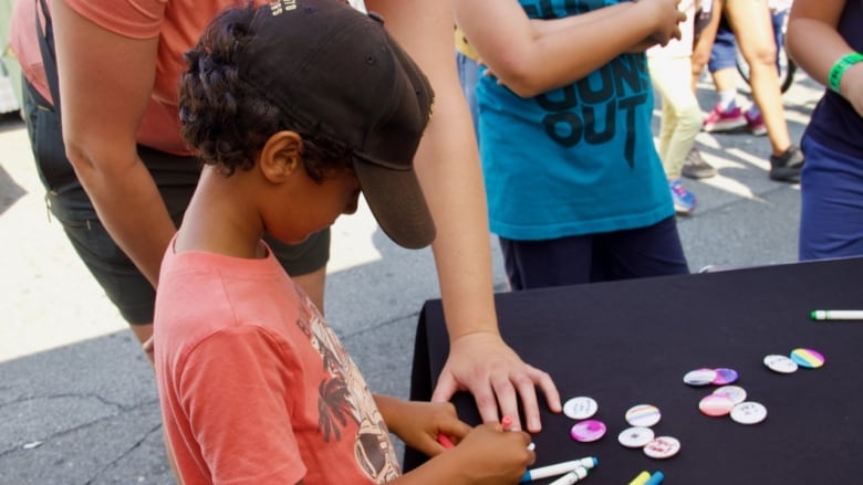 A child colours a button at a table outdoors