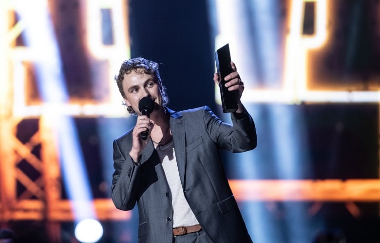 A young man in a grey suit lifts his award in the air.