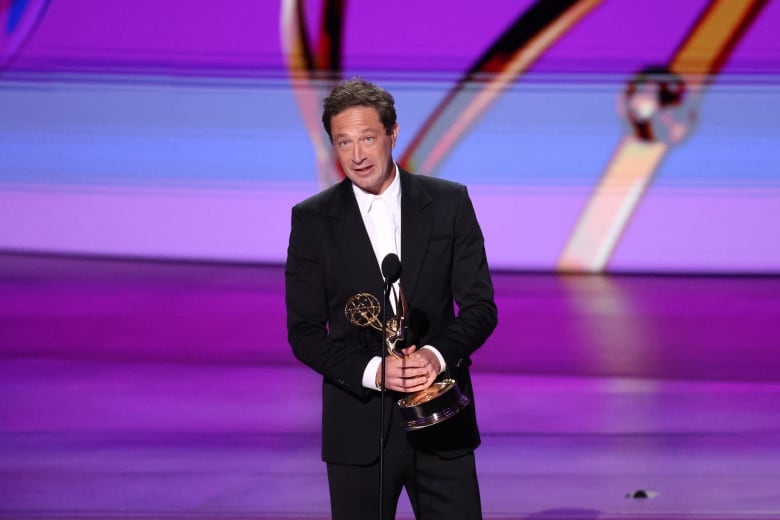 A person holding an award delivers a speech onstage.